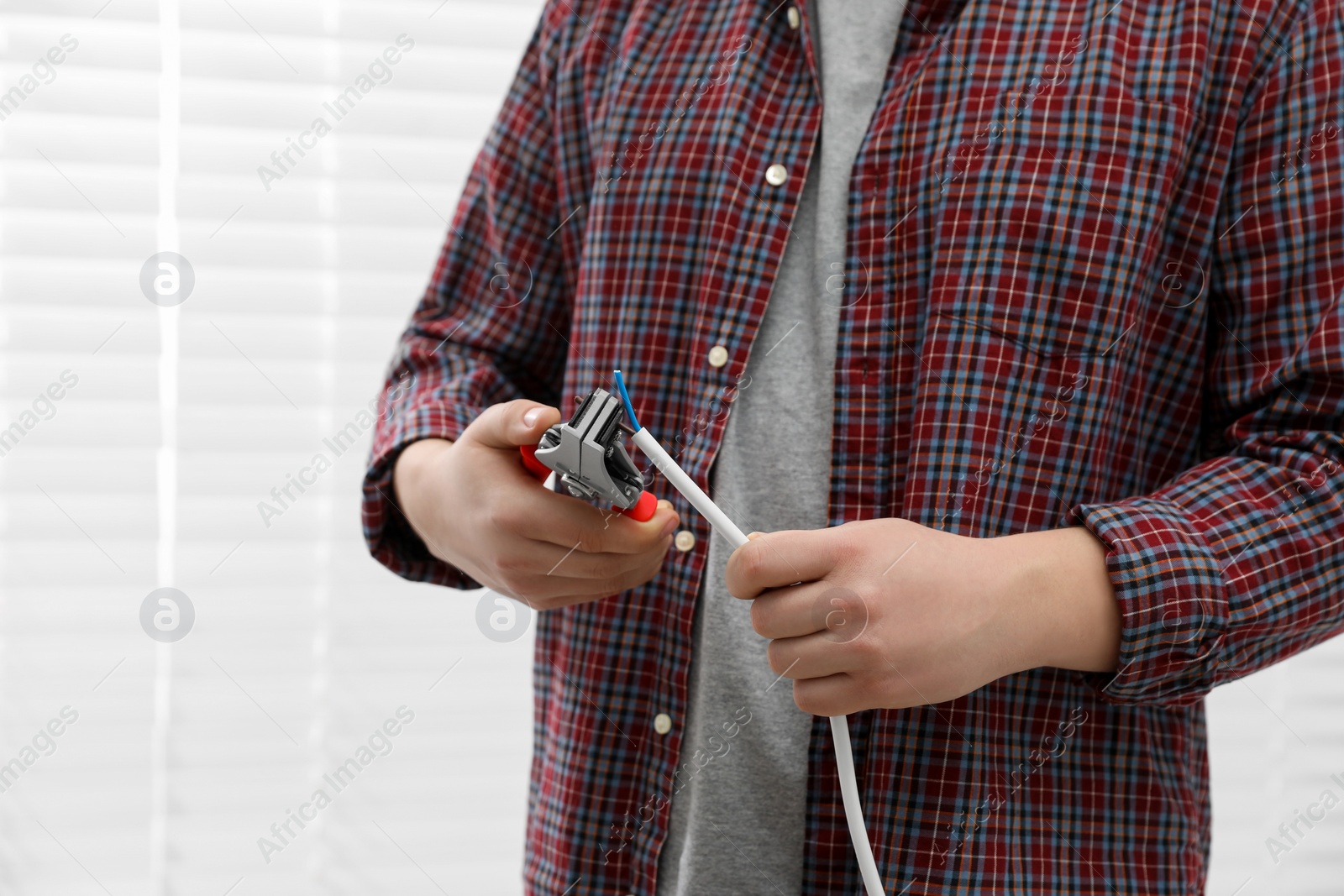 Photo of Professional electrician stripping wiring indoors, closeup view