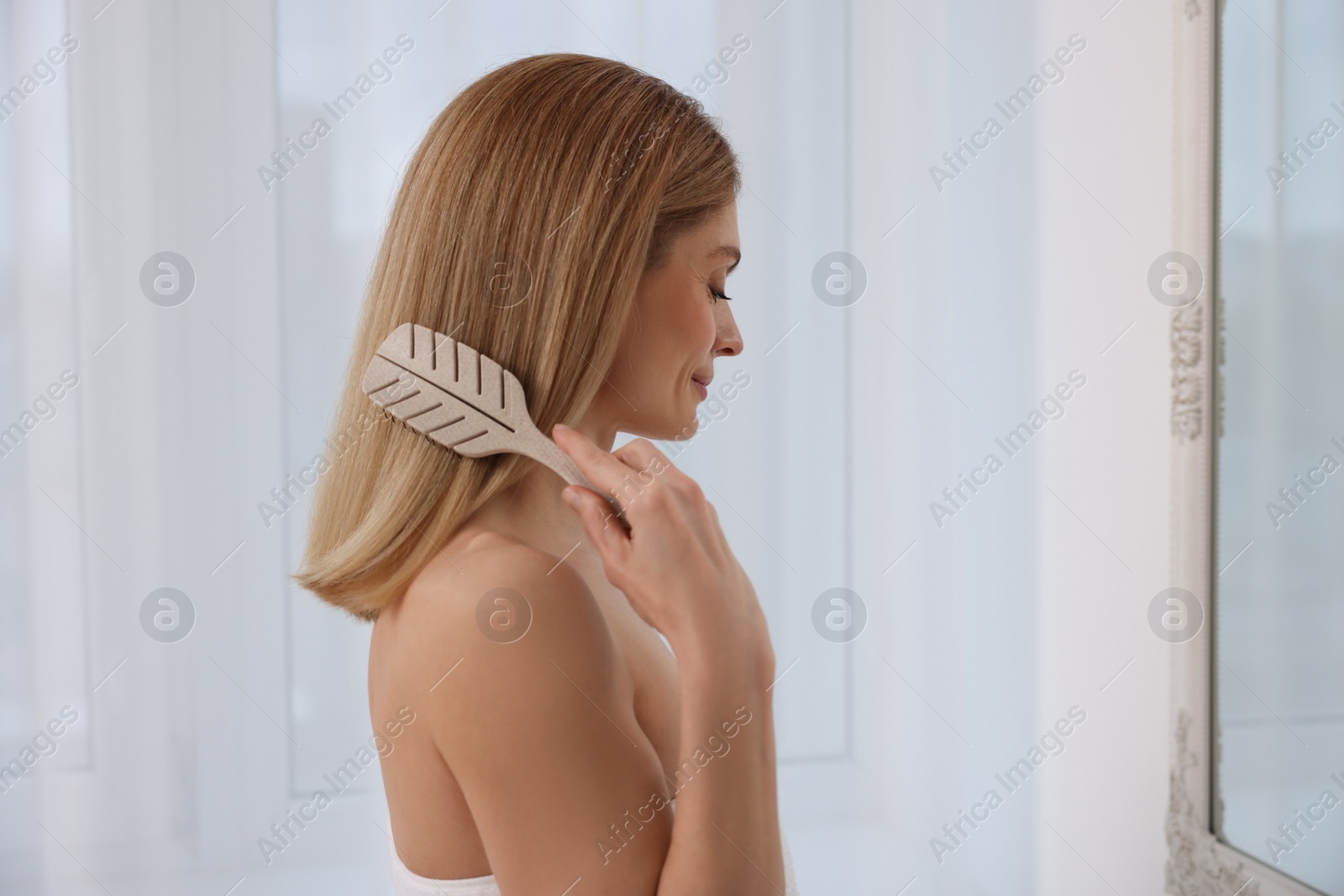 Photo of Beautiful woman brushing her hair near mirror in room