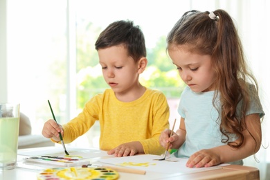 Photo of Cute little boy and girl drawing at table in living room