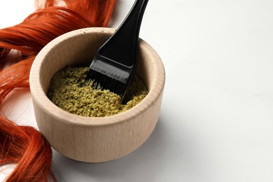 Photo of Henna powder, brush and red strand on white table, closeup with space for text. Natural hair coloring