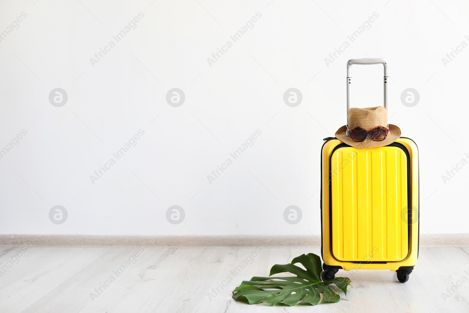 Photo of Bright yellow suitcase with hat and sunglasses near light wall indoors