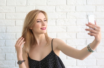 Photo of Attractive young woman taking selfie near brick wall