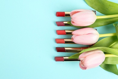 Photo of Bright lipsticks and spring flowers on light blue background, flat lay. Space for text