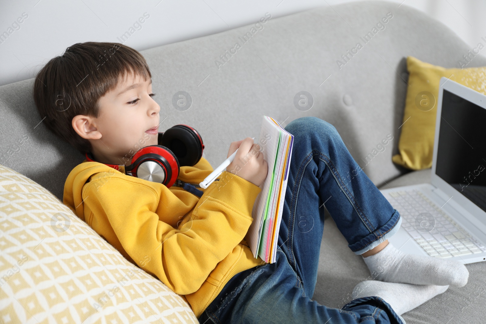 Photo of Cute little boy with modern laptop studying online at home. E-learning