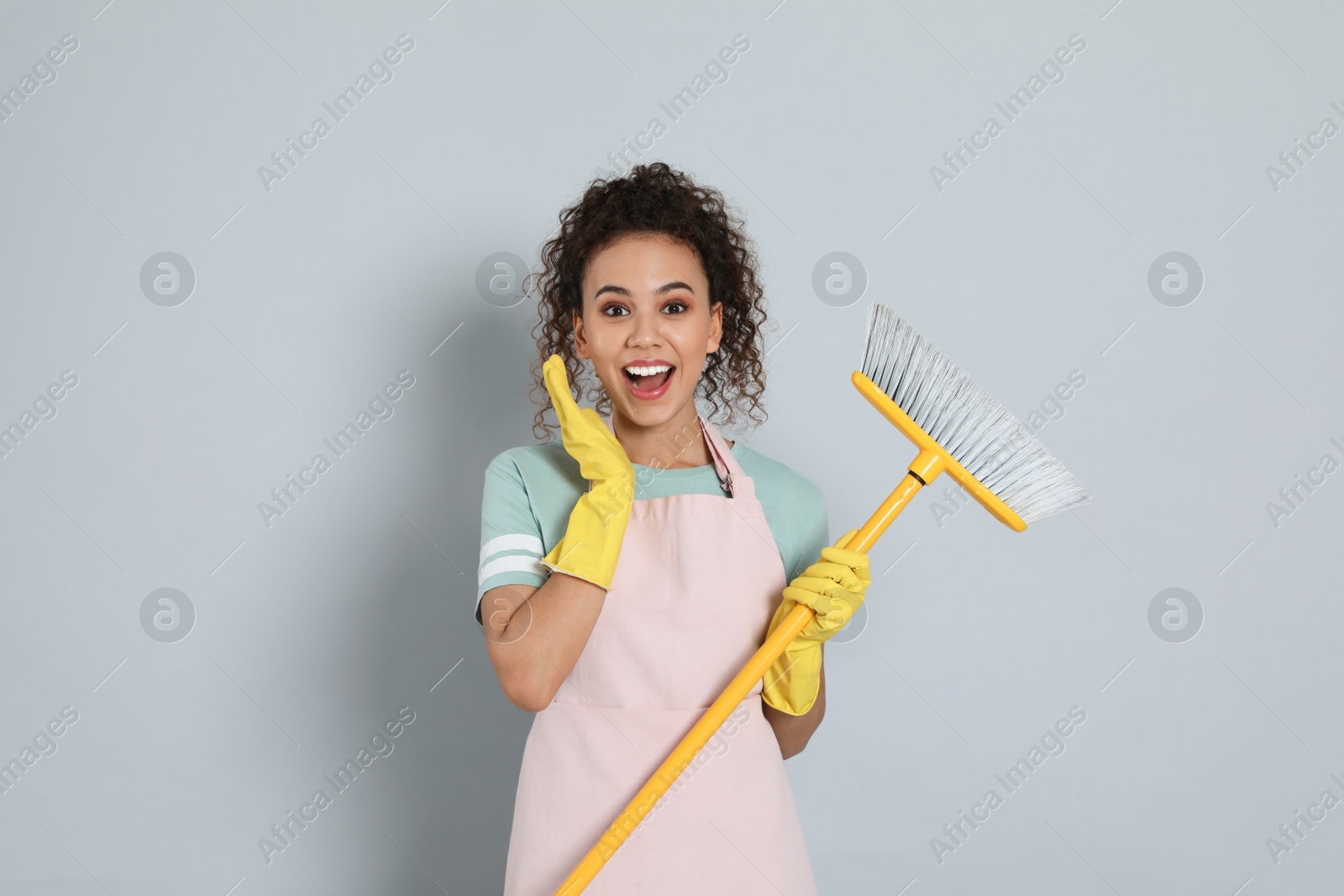 Photo of Emotional African American woman with yellow broom on grey background