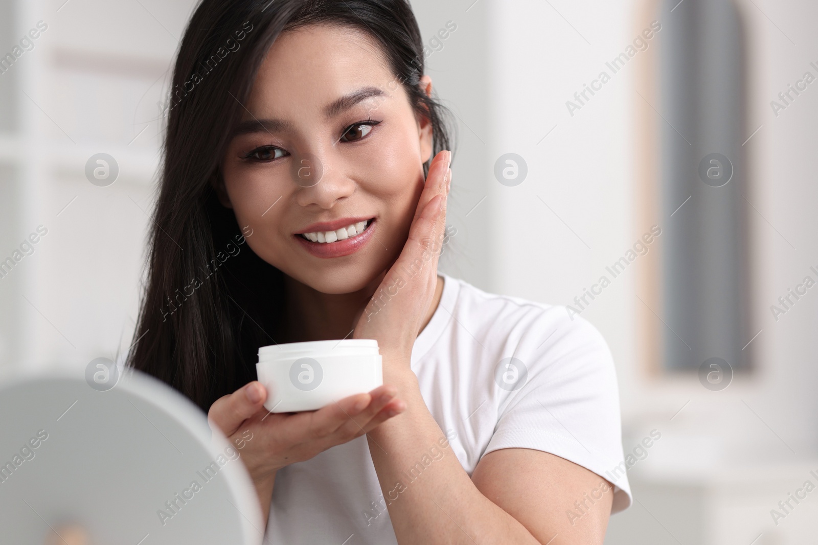 Photo of Happy woman applying face cream at home, space for text