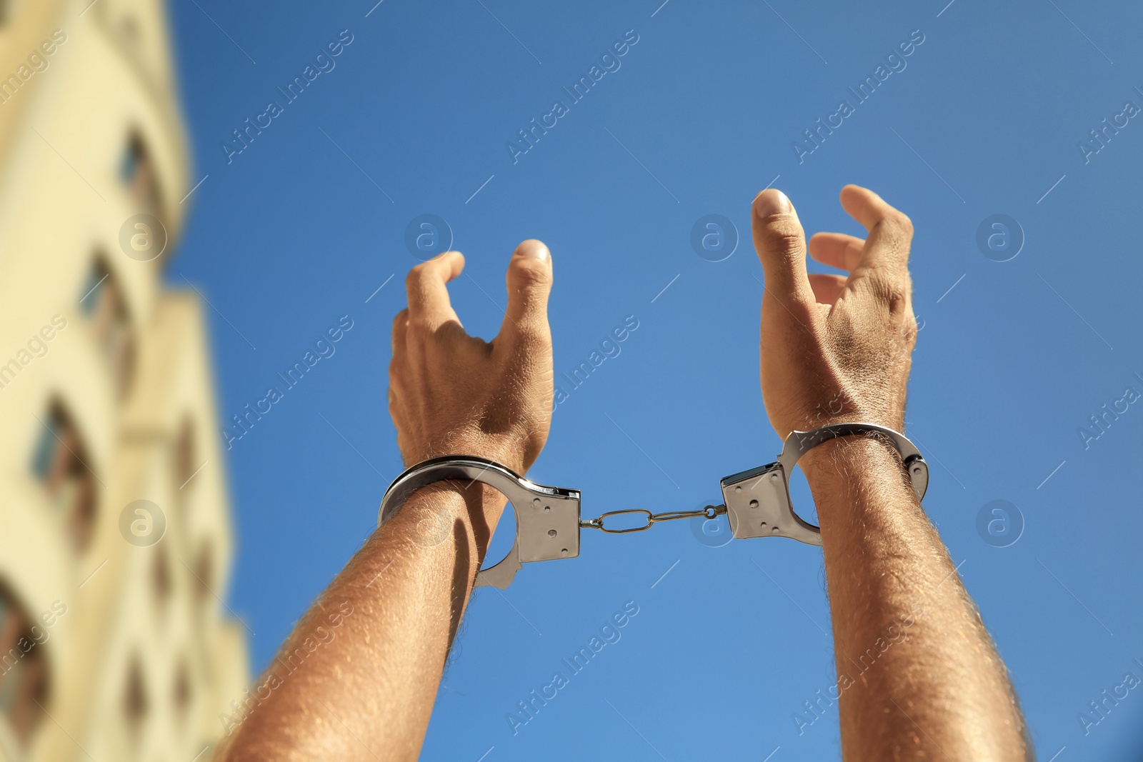 Photo of Man in handcuffs against blue sky outdoors, closeup