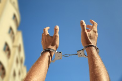 Man in handcuffs against blue sky outdoors, closeup