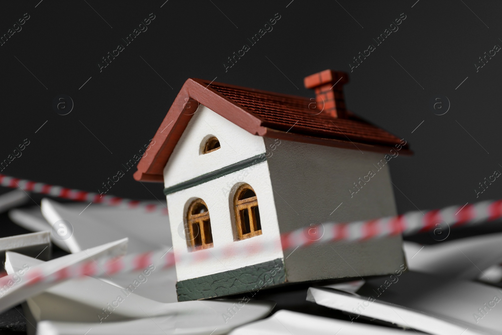 Photo of House model and broken dishes on black table depicting destruction after earthquake, closeup