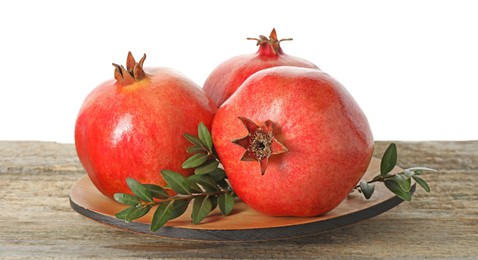 Fresh pomegranates and green leaves on wooden table against white background