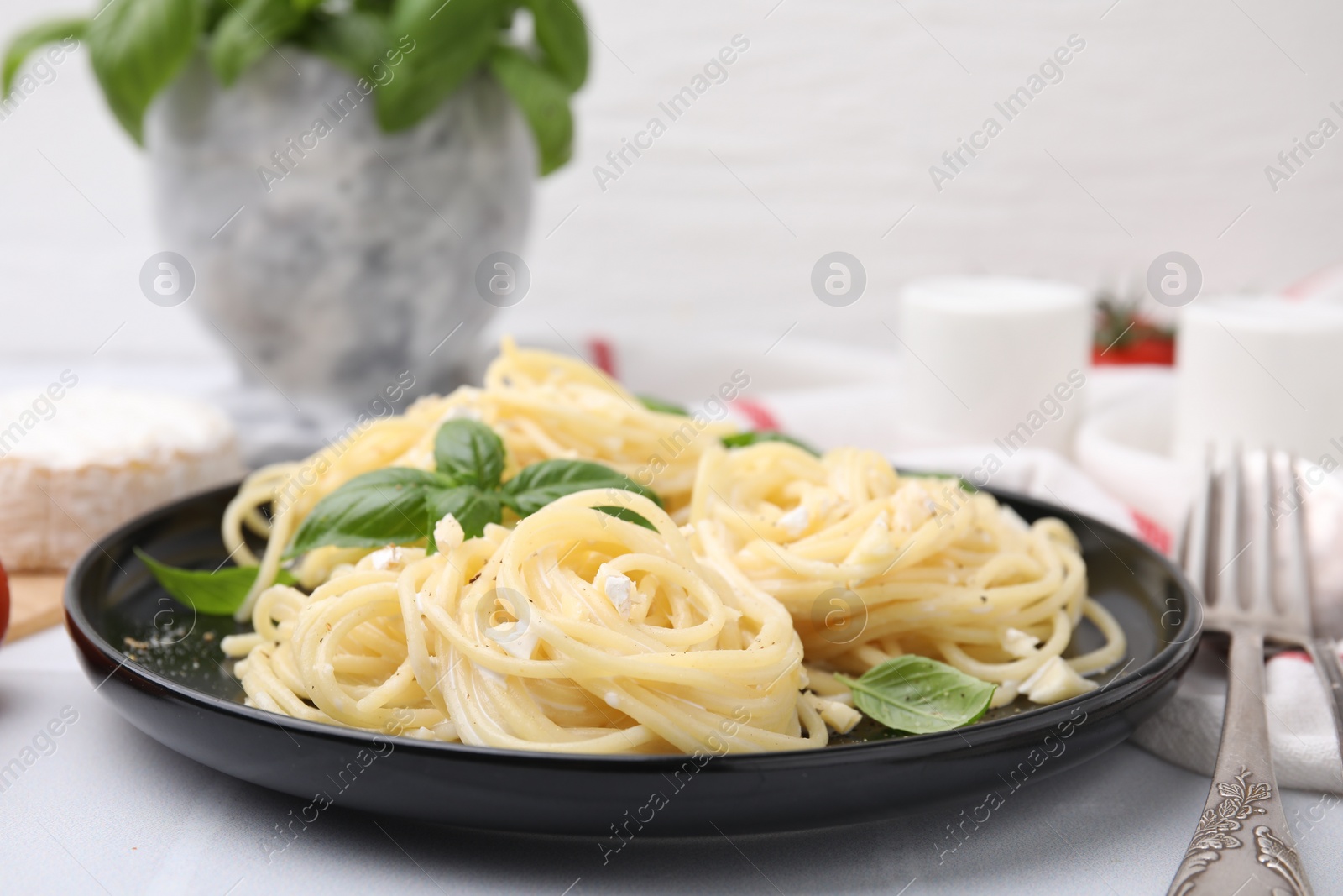 Photo of Delicious pasta with brie cheese and basil leaves on white table, closeup