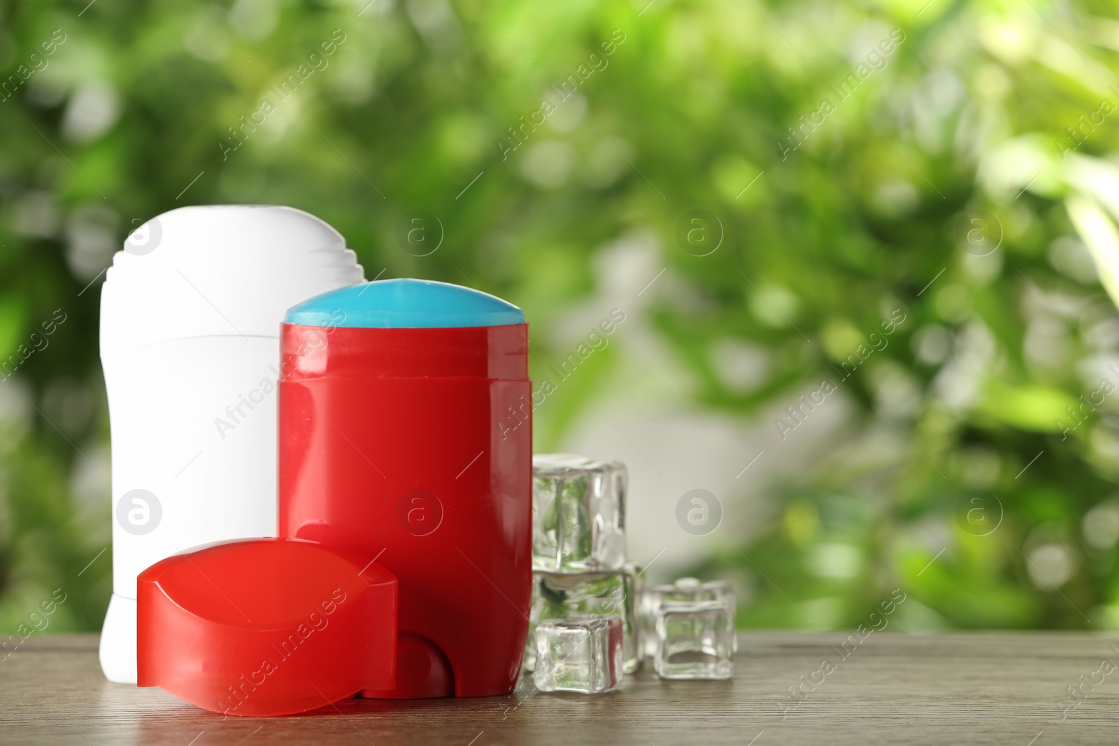 Photo of Different deodorants and ice cubes on wooden table against blurred background. Space for text