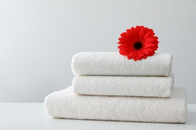 Photo of Stack of fresh towels with flower on table against white background. Space for text