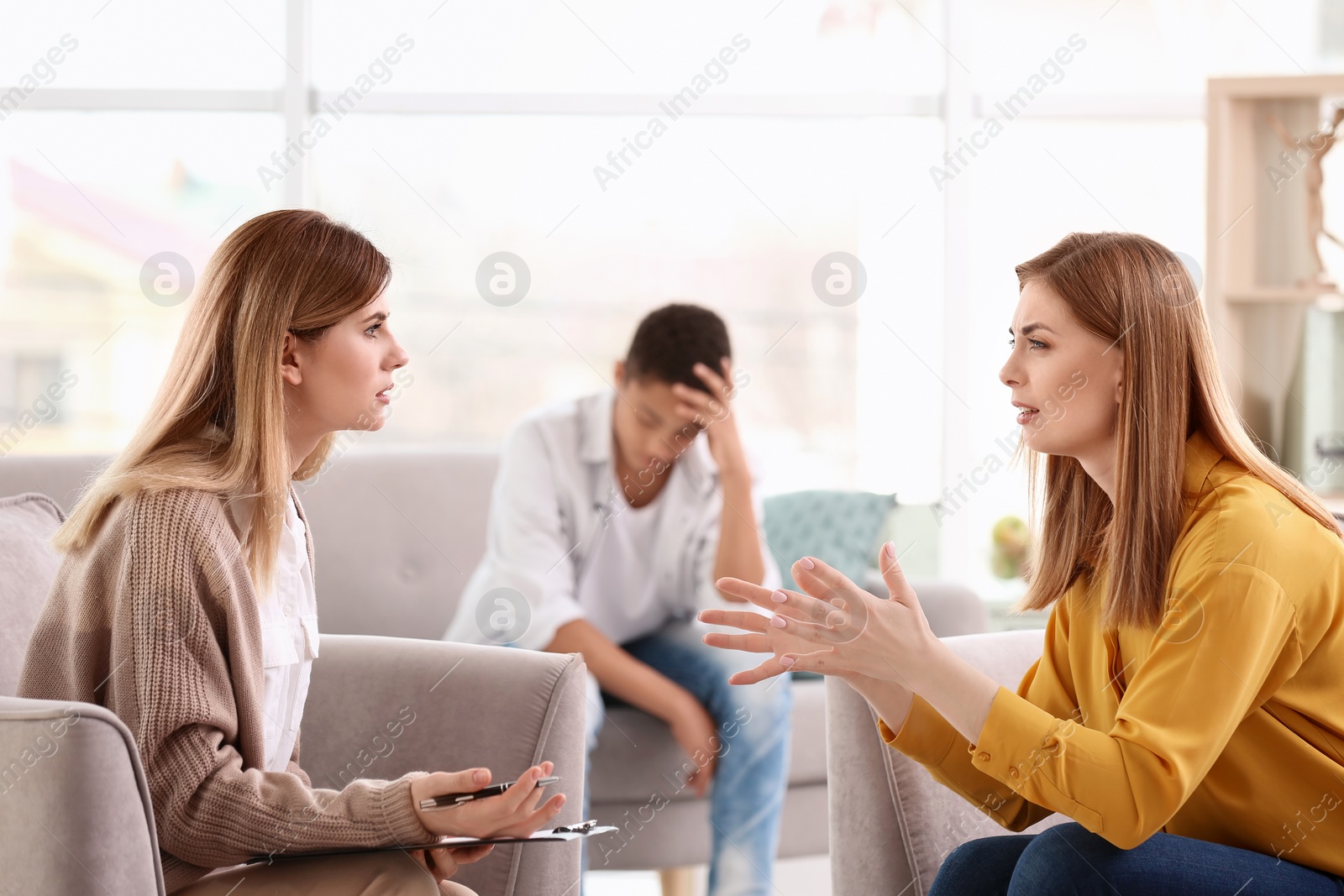 Photo of Young female psychologist working with teenage boy and his mother in office