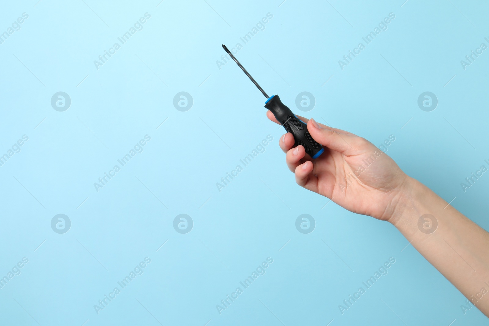 Photo of Woman holding screwdriver on light blue background, closeup. Space for text