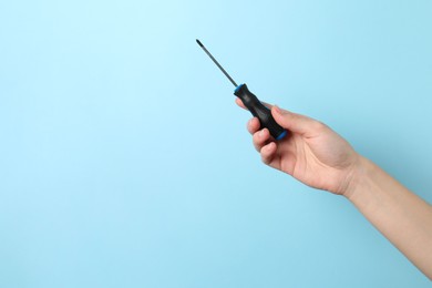 Photo of Woman holding screwdriver on light blue background, closeup. Space for text