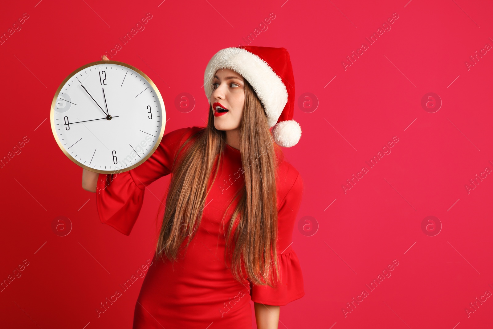 Photo of Young beautiful woman in Santa hat holding big clock on color background. Christmas celebration