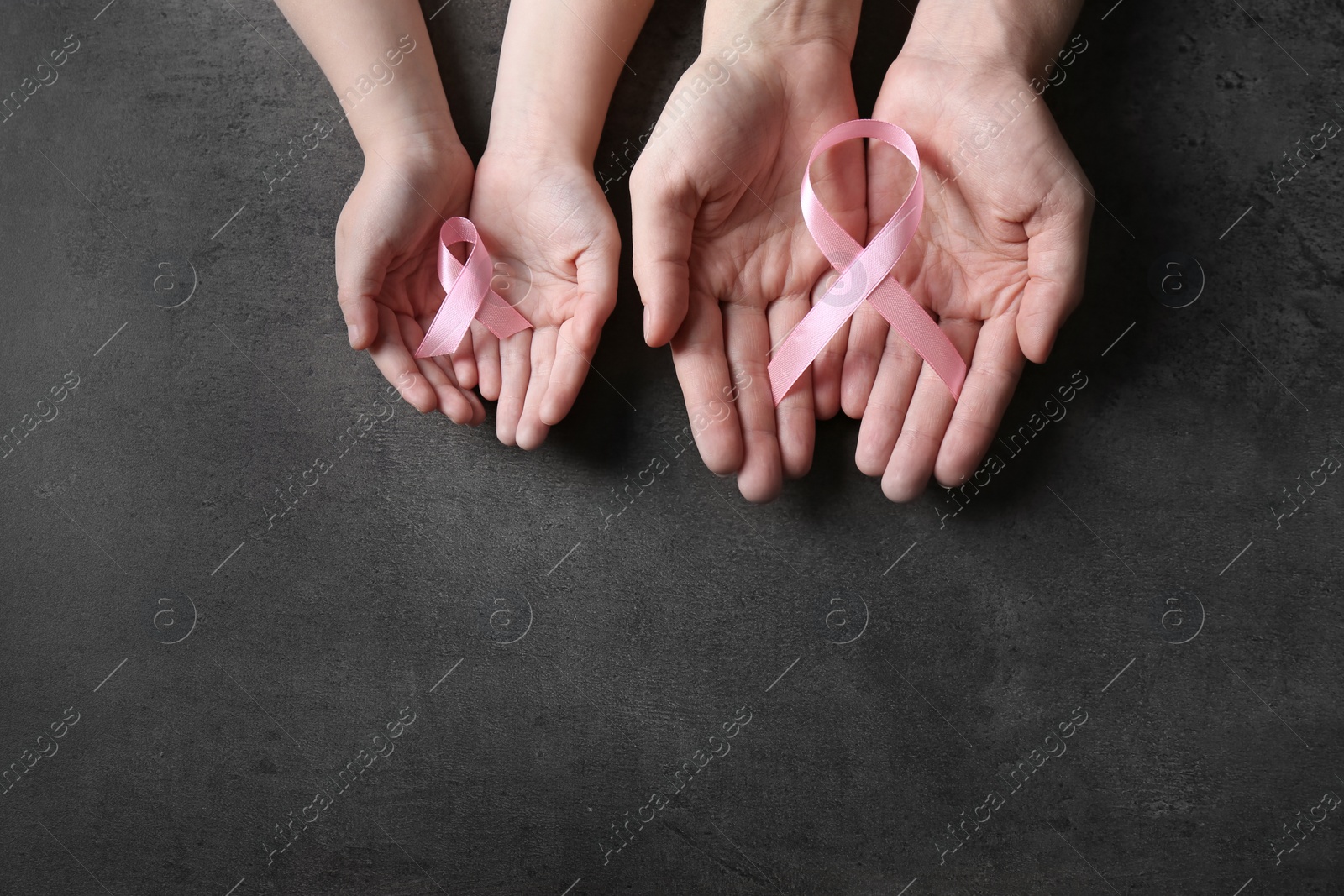 Photo of Woman and girl holding pink ribbons on grey background, top view with space for text. Breast cancer awareness