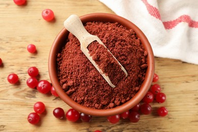 Photo of Cranberry powder in bowl, scoop and fresh berries on wooden table, top view