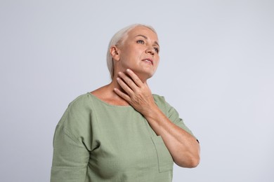 Photo of Mature woman doing thyroid self examination on light grey background