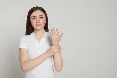 Photo of Young woman suffering from pain in her hand on light grey background, space for text. Arthritis symptoms
