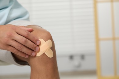 Photo of Man putting sticking plasters onto knee indoors, closeup. Space for text