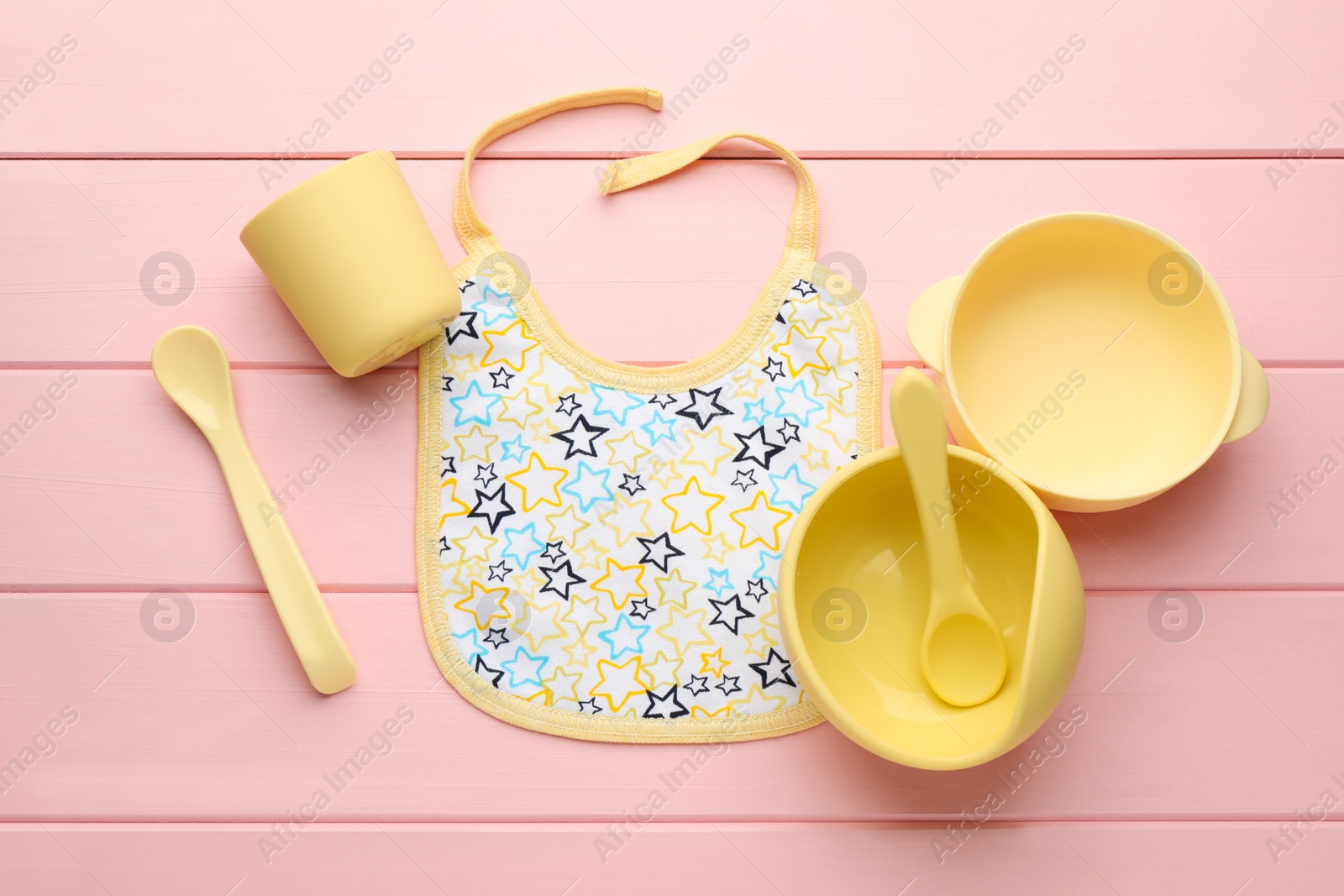 Photo of Flat lay composition with drool baby bib and plastic dishware on pink wooden background