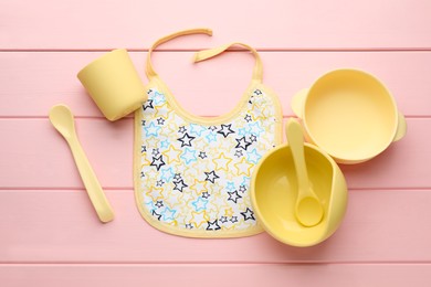 Flat lay composition with drool baby bib and plastic dishware on pink wooden background