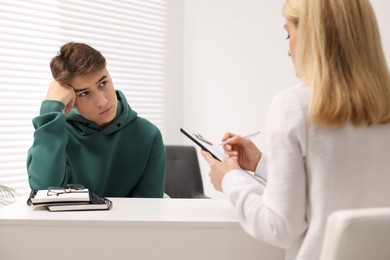 Psychologist working with teenage boy at table in office