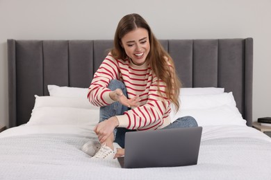 Photo of Happy woman with laptop on bed in bedroom