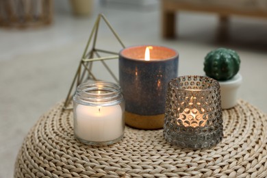 Lit candles and decor elements on wicker pouf indoors