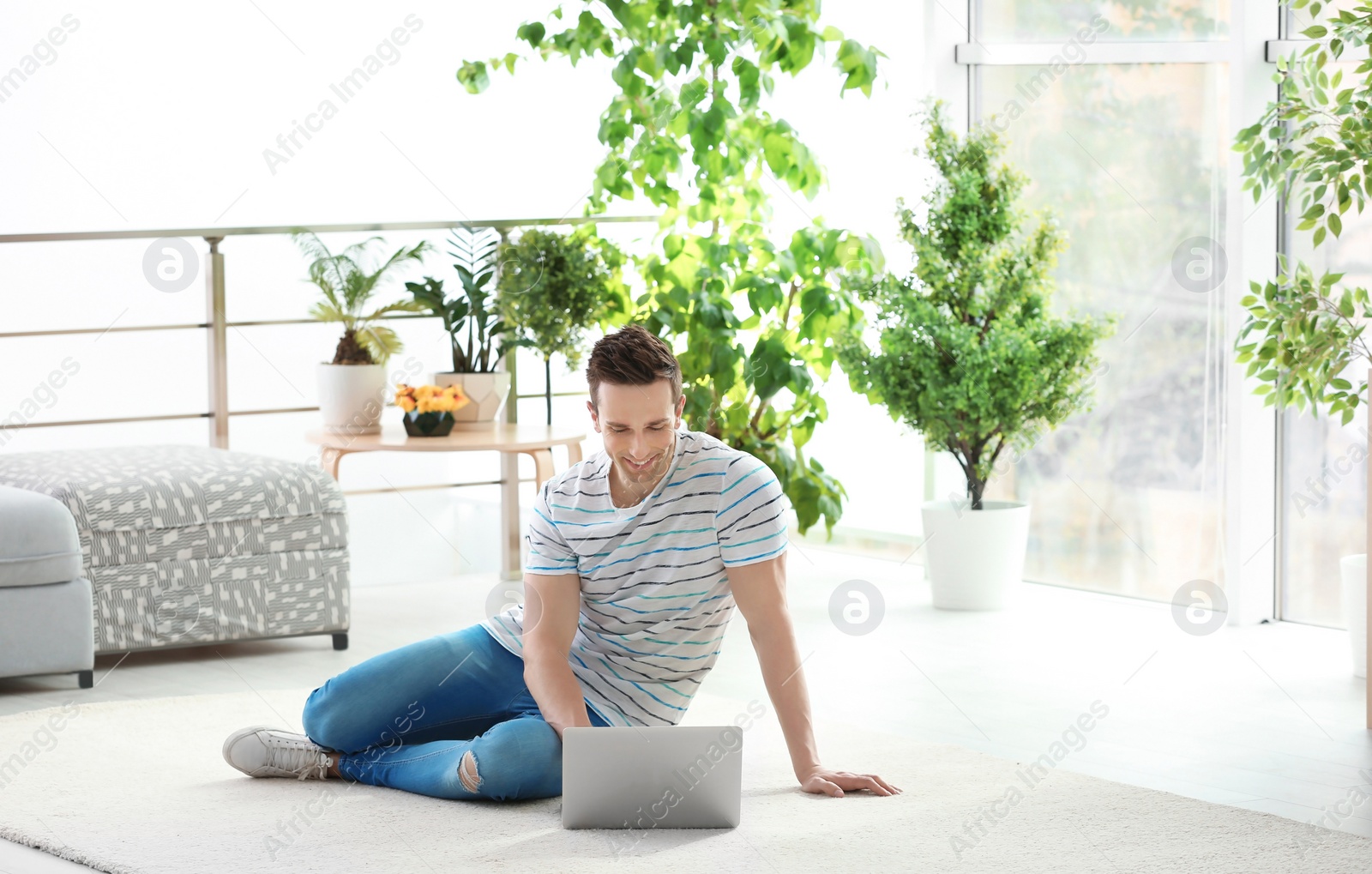 Photo of Handsome young man working with laptop on cozy carpet at home