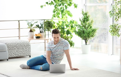 Handsome young man working with laptop on cozy carpet at home