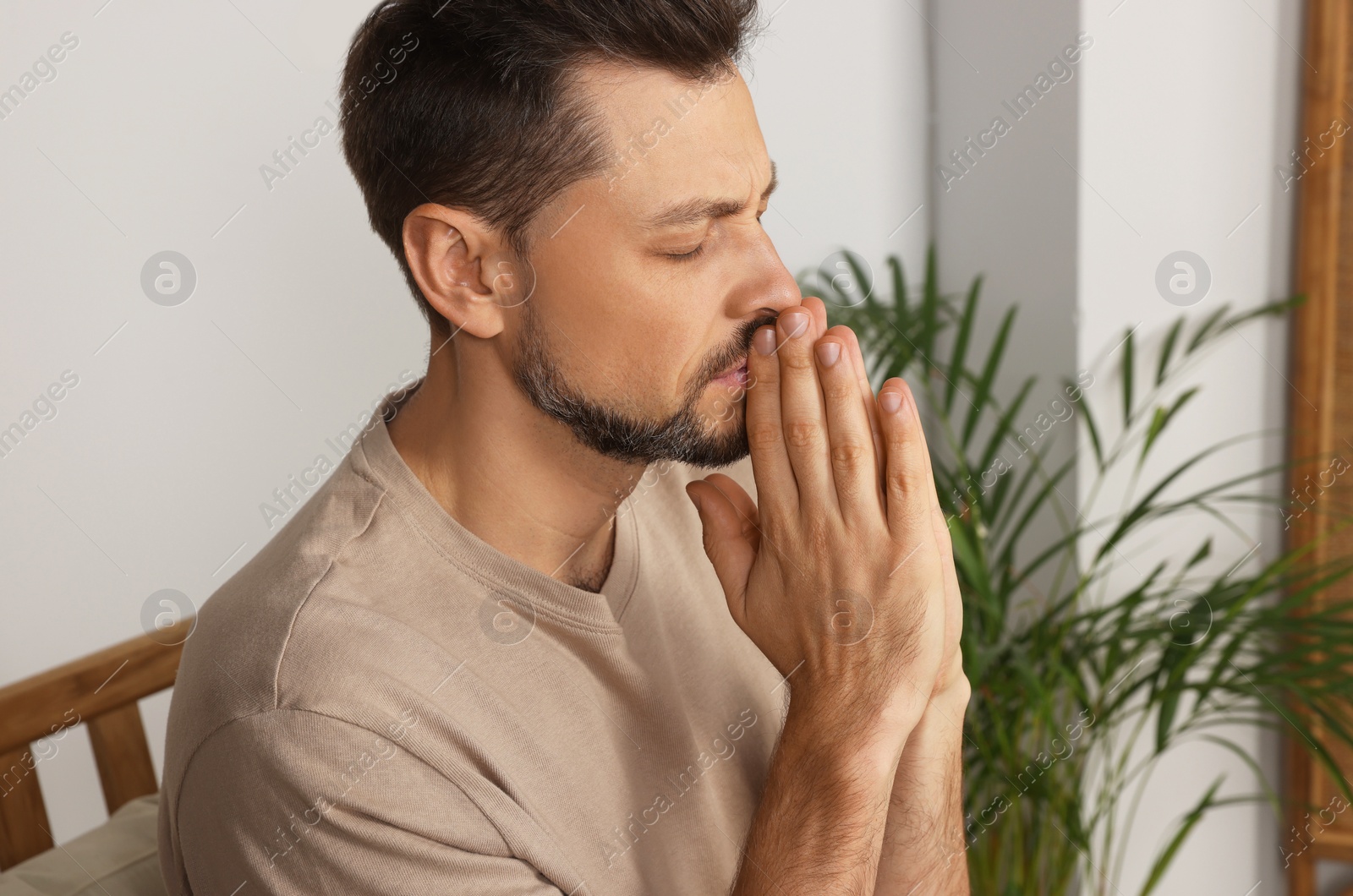 Photo of Man with clasped hands praying in room at home