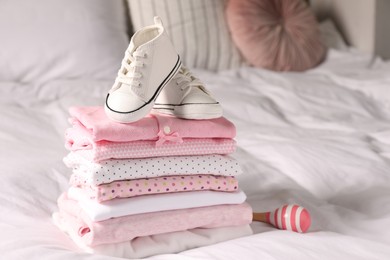 Photo of Stack of baby girl's clothes, rattle and shoes on bed. Space for text