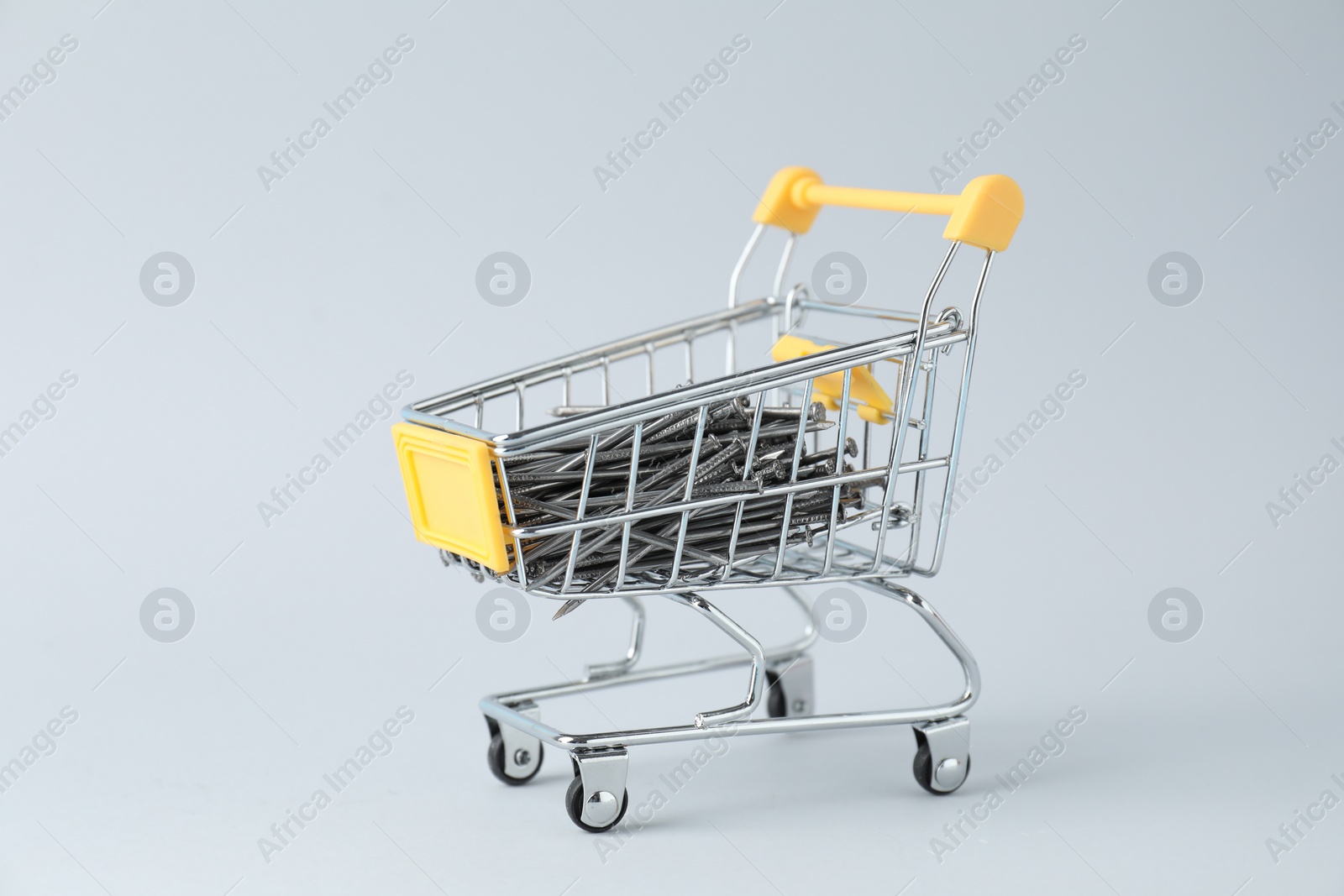 Photo of Metal nails in shopping cart on light grey background