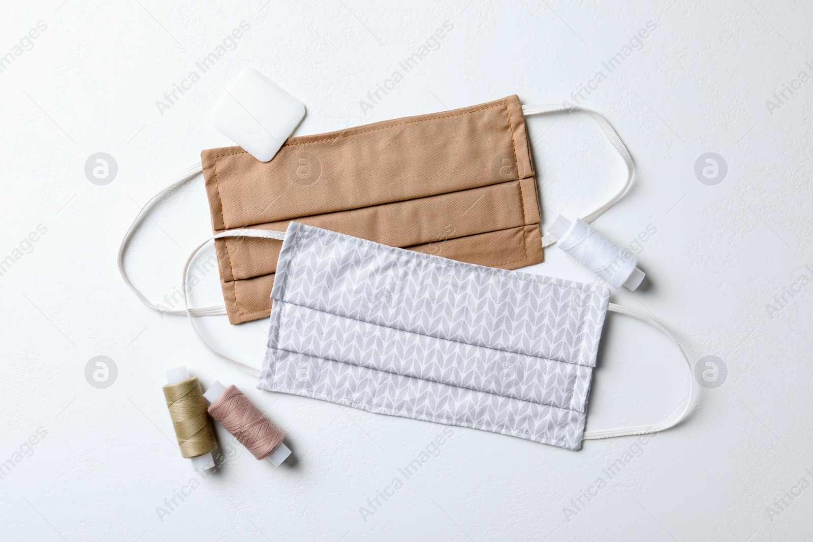 Photo of Homemade protective masks, threads and tailor's chalk on white background, flat lay. Sewing idea