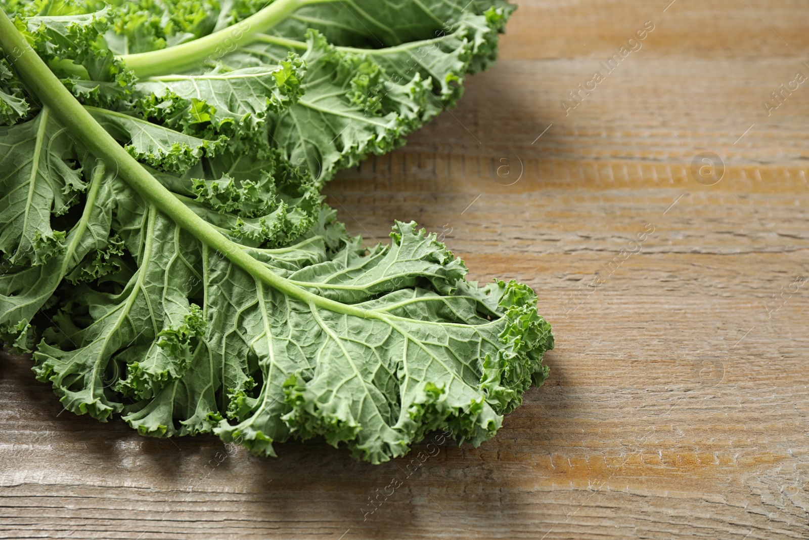 Photo of Fresh green kale leaves on wooden table, closeup