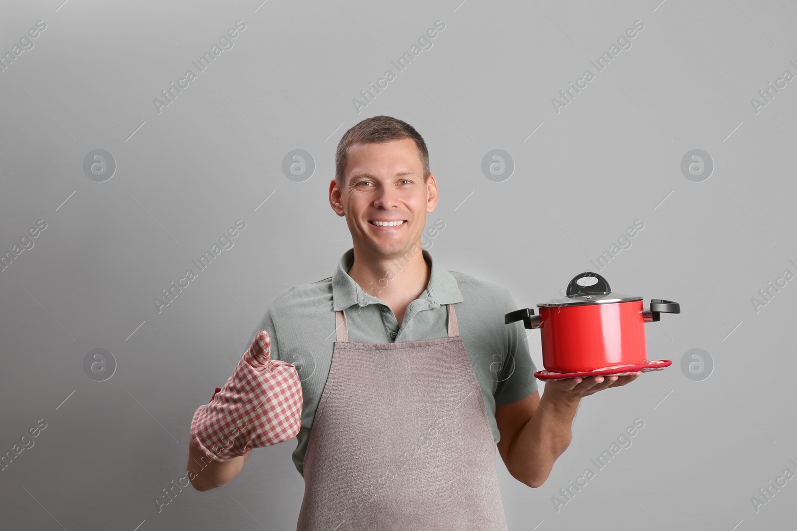 Photo of Happy man with cooking pot on light grey background