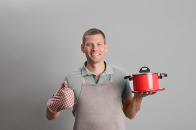 Happy man with cooking pot on light grey background