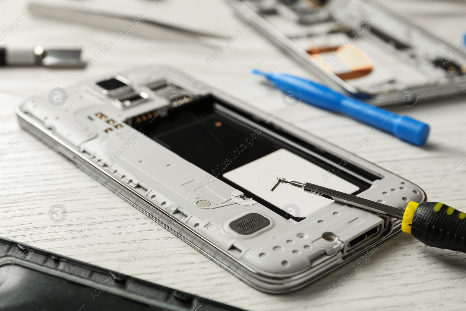 Photo of Damaged smartphone and repair tool on wooden background, closeup