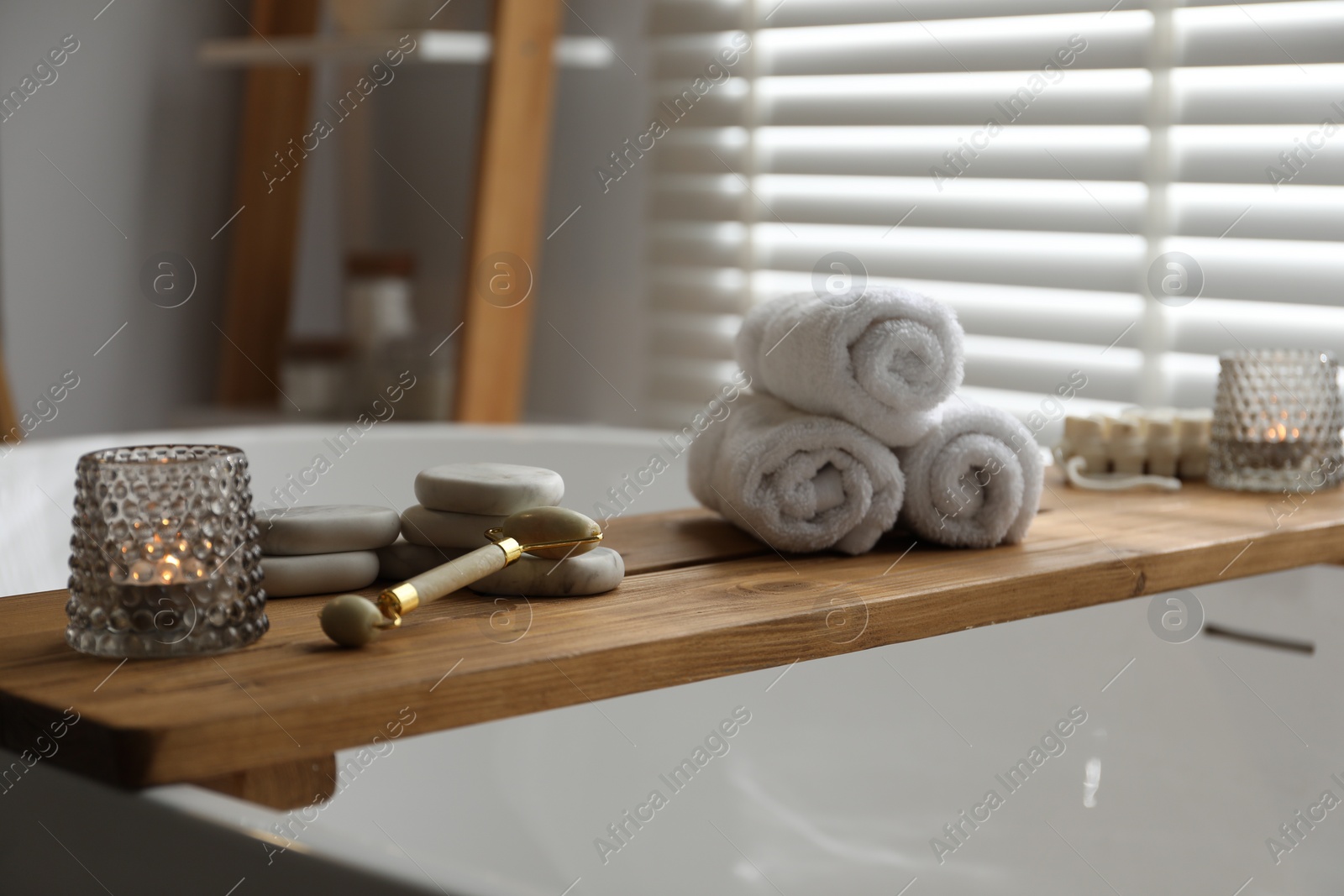 Photo of Wooden tray with spa products and burning candles on bath tub in bathroom
