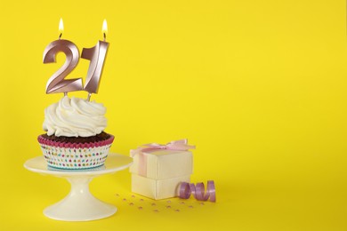Delicious cupcake with number shaped candles on yellow background, space for text. Coming of age party - 21th birthday