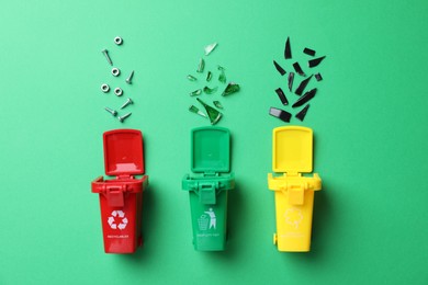 Mini recycling bins and different garbage on green background, flat lay. Waste sorting