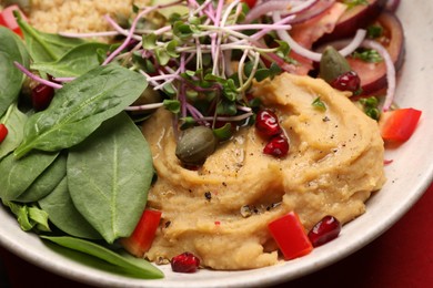 Photo of Delicious vegan bowl with microgreens, spinach and hummus on red tablecloth, closeup