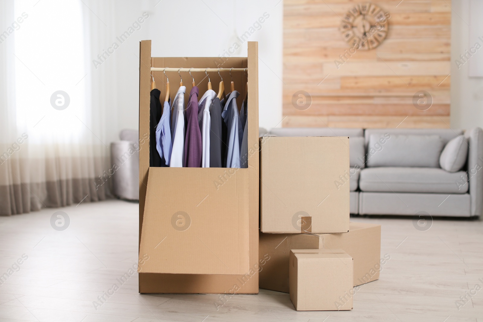 Photo of Cardboard wardrobe box with clothes on hangers in living room