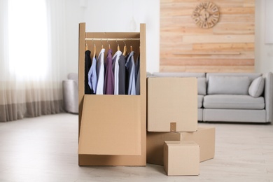 Cardboard wardrobe box with clothes on hangers in living room