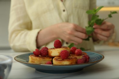 Photo of Woman decorating delicious cottage cheese pancakes with fresh mint at white table, closeup