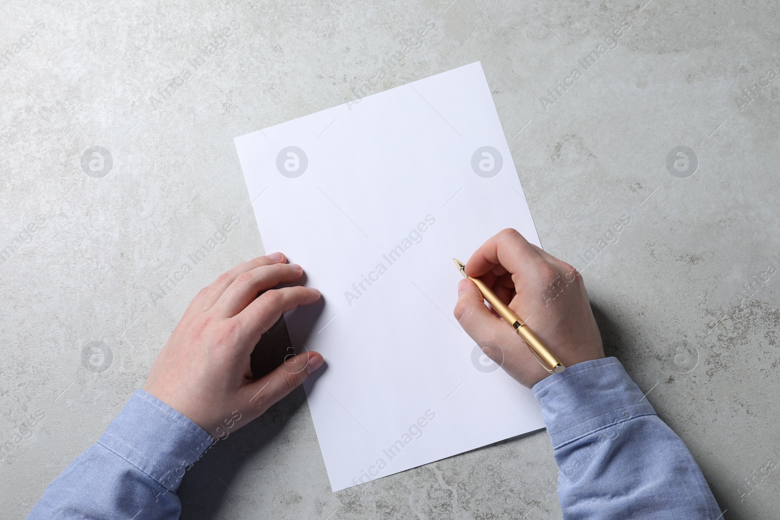 Photo of Man writing on sheet of paper with pen at light grey table, top view