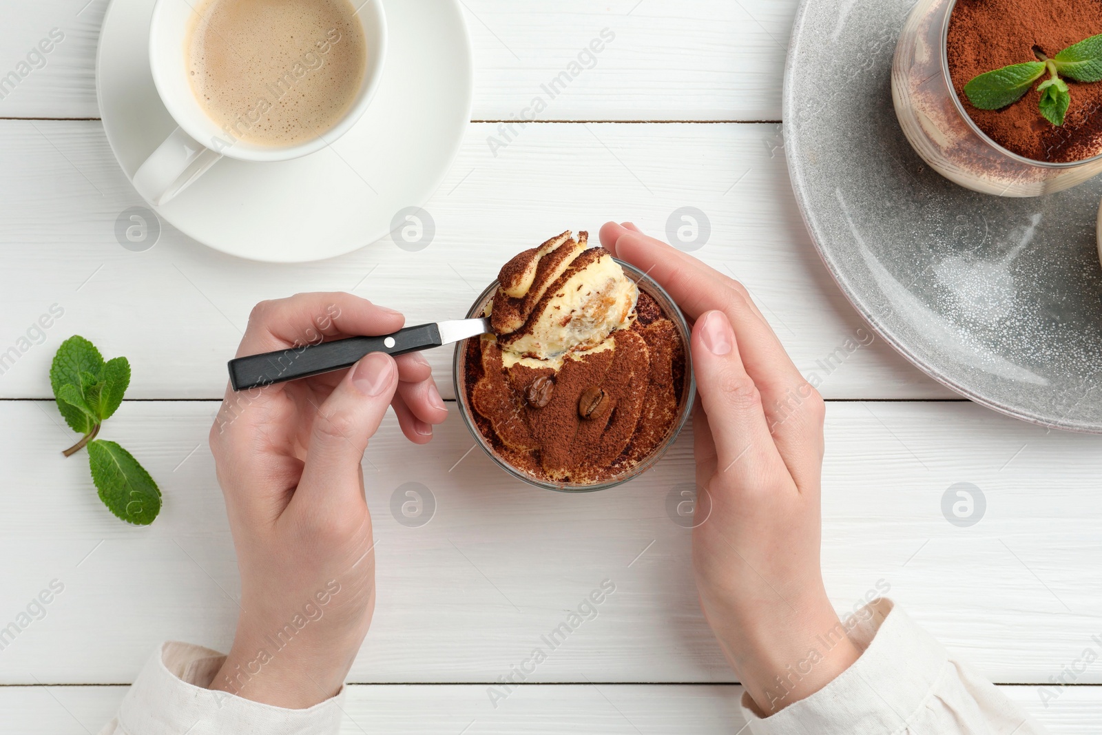 Photo of Woman eating delicious tiramisu at white wooden table, top view